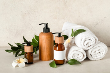 Composition with bottles of shampoo, towels and flowers on table near beige grunge wall