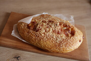 Golden khachapuri with a crispy crust sprinkled with cheese, filled with mozzarella cheese, served on a wooden board with parchment paper. Perfect for advertising bakeries, cooking blogs, or restauran