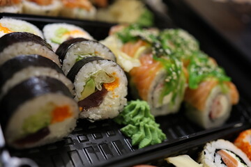A vibrant assortment of sushi rolls with salmon, avocado, and caviar, served in a black tray with wasabi. Perfect for Japanese cuisine ads, food blogs, or restaurant menus. 