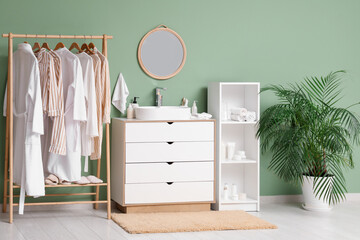Rack with clothes, chest of drawers and shelving unit near green wall in room