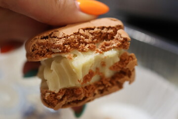 Close-up of a hand holding a bitten macaron with a creamy filling and a crispy texture. Perfect for dessert blogs, bakery advertising, or food photography. 