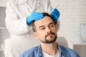 Trichologist marking man's head with hair loss problem in clinic, closeup