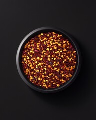 A black bowl filled with vibrant red and orange chili flakes set against a dark background.