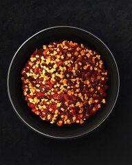 A vibrant bowl of chili flakes, showcasing a mix of red and yellow hues against a dark background.