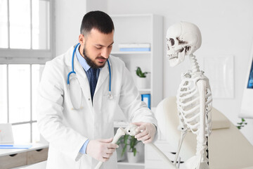 Fototapeta premium Male doctor examining knee joint of human skeleton model in clinic