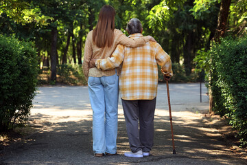 Obraz premium Senior woman with stick and caregiver hugging in park, back view