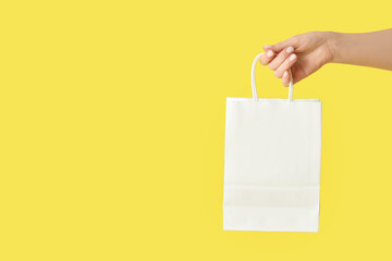 Female hand with paper shopping bag on yellow background