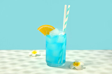 Glass of tasty Blue Lagoon cocktail garnished with orange and plumeria flowers on white table against color background