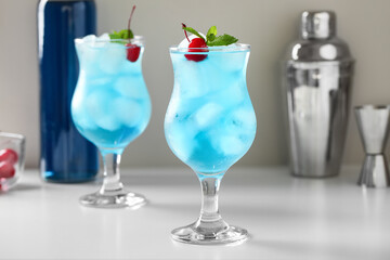 Glasses of tasty Blue Lagoon cocktail garnished with cherries and mint on white background