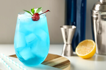 Glass of tasty Blue Lagoon cocktail garnished with cherry and mint on white background