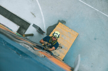 
Firefighter rescuer descending a massive wall using a rappelling device in a multi-story building, wearing protective gear such as a helmet, harness, and carabiners.