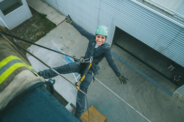 Female firefighter rescuer descending a huge wall with the rappelling device in a multi-story building, hanging without hands and smiling at the camera.