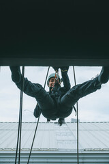 Female firefighter rescuer descending a huge wall with the rappelling device in a multi-story building, hanging from a window.