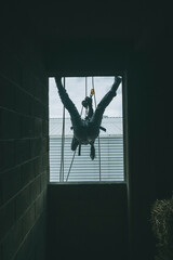Female firefighter rescuer descending a huge wall with the rappelling device in a multi-story building, hanging from a window.