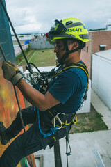 
Firefighter rescuer descending a massive wall using a rappelling device in a multi-story building, wearing protective gear such as a helmet, harness, and carabiners.