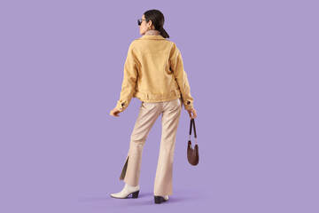 Fototapeta premium Young woman in stylish jacket on lilac background, back view
