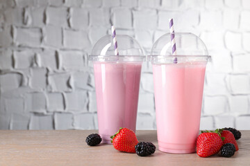 Tasty milkshakes in plastic cups and fresh berries on wooden table, closeup