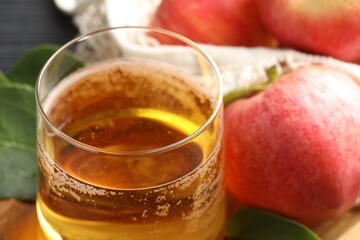 Fresh cider in glass, apples and green leaves on table, closeup