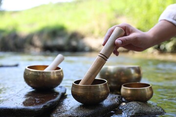 Woman with singing bowls by river, closeup