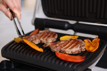 Man cooking meat and vegetables on electric grill in kitchen, closeup