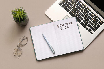 Notebook with text NEW YEAR 2026 and laptop on grey background