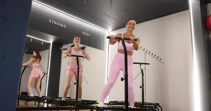 Smiling women training on mini exercise trampolines in fitness studio, low angle view