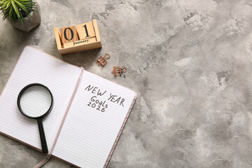 Notebook with text NEW YEAR GOALS 2026, calendar and magnifying glass on grey grunge table