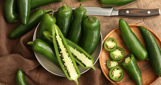 Ripe green jalapeno peppers and knife on wooden table, spinning. Top view