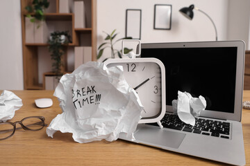 Crumpled paper with text BREAK TIME, alarm clock and laptop on desk in office