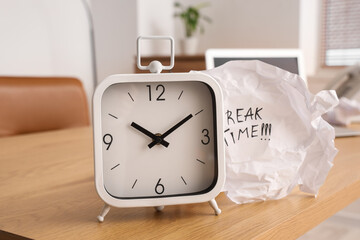 Crumpled paper with text BREAK TIME and alarm clock on desk in office, closeup