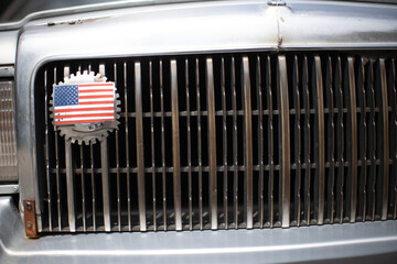 American Patriotism: Vintage Car Front with US Flag Gear Emblem on Grille, Close-Up