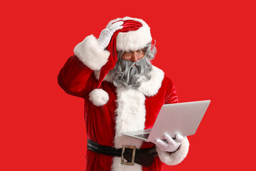 Shocked Santa Claus with laptop on red background