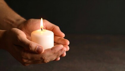 Holding a lit candle in hands during a quiet moment of reflection in a dimly lit room