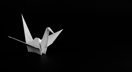 A pristine white origami crane appears elegant against the stark, vast black background, showcasing delicate details of handcrafted paper bird. Funeral concept. Copy space.