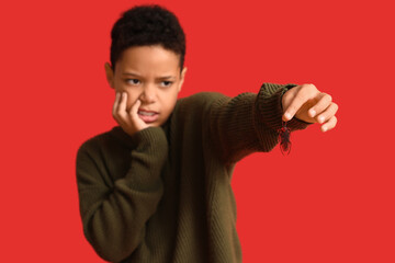 Scared African-American boy with cockroach on red background, closeup