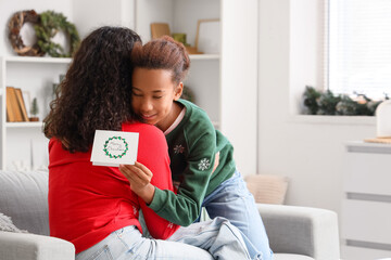 African-American mother and her daughter with greeting card hugging at home on Christmas eve