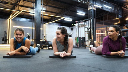 Three latin hispanic women lying on mats, smiling and resting after their fitness workout in a modern gym