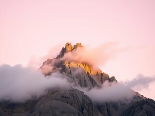 Fototapeta premium Majestic mountain peak bathed in warm golden sunrise light surrounded by soft pink clouds and mist