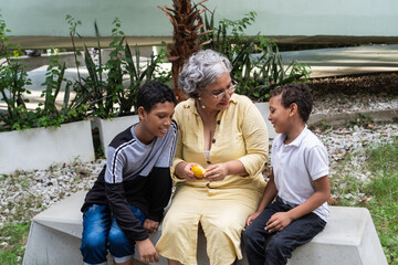 Fototapeta premium Grandmother sharing fruit with grandsons outdoors