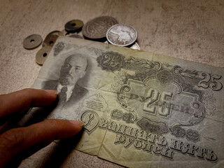 Banknote collection hand presents a 25 ruble lenin banknote and coins for numismatic appraisal.