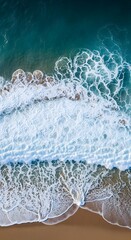 Naklejka premium High-angle view of foamy waves crashing on a sandy beach.