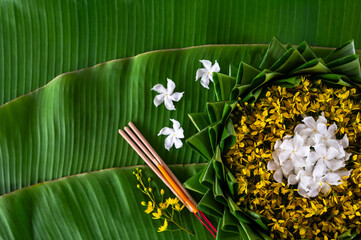 Krathong decorates with flowers that have blurred focus of 3 incense sticks and candle put on banana leaf for Loy Krathong festival.