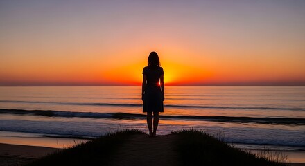 Fototapeta premium Woman silhouetted against vibrant sunset at the beach.