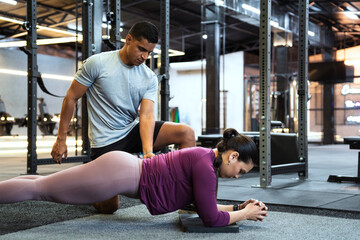 Determined sportswoman practicing plank exercise with personal trainer assisting, focusing on fitness and core strength in modern gym setting