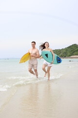 Fototapeta premium Couple lover running on beach with surfboards, splashing water and smiling under summer sunlight, concept of friendship, vacation, holidays, surfing, freedom, and fun tropical lifestyle. 