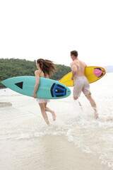 Obraz premium Couple lover running on beach with surfboards, splashing water and smiling under summer sunlight, concept of friendship, vacation, holidays, surfing, freedom, and fun tropical lifestyle. 