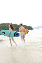 Obraz premium Couple lover running on beach with surfboards, splashing water and smiling under summer sunlight, concept of friendship, vacation, holidays, surfing, freedom, and fun tropical lifestyle. 