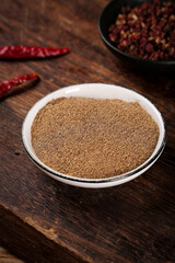 Ground Red Pepper Powder in White Bowl with Dried Chilies and Peppercorns on Wood Table