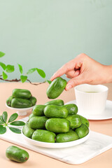 Fresh Baby Kiwi Fruits on White Plate with Hand Picking Small Green Fruit in Light Natural Setting