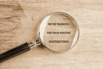 A magnifying glass rests on a textured wooden surface, magnifying the message expressing gratitude for positive contributions. This setting creates a thoughtful atmosphere of appreciation